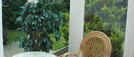 Un invernadero con una mesa y sillas de mimbre, una planta en maceta y vistas a un jardín.