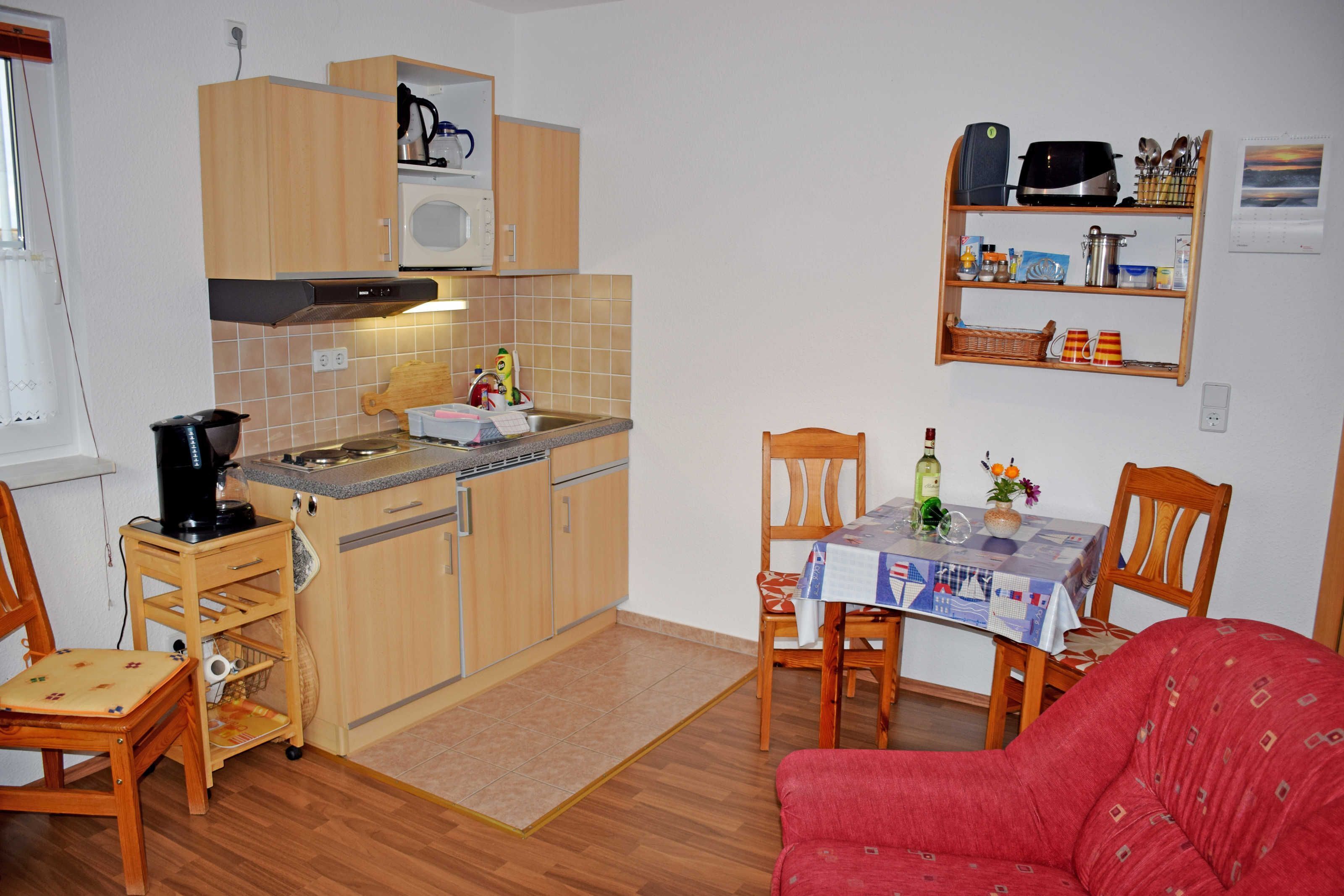 Une cuisine compacte avec des meubles en bois, un four à micro-ondes et une machine à café. On y trouve une table à manger avec des chaises et un canapé rouge.
