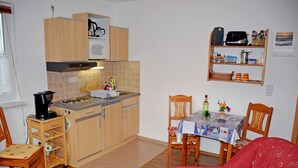 A compact kitchen with wooden cabinets, a microwave, and a coffee maker. There is a dining table with chairs and a red sofa. - Vacation apartment Mönchgut - Holiday apartments in Gager on Rügen (Gager)