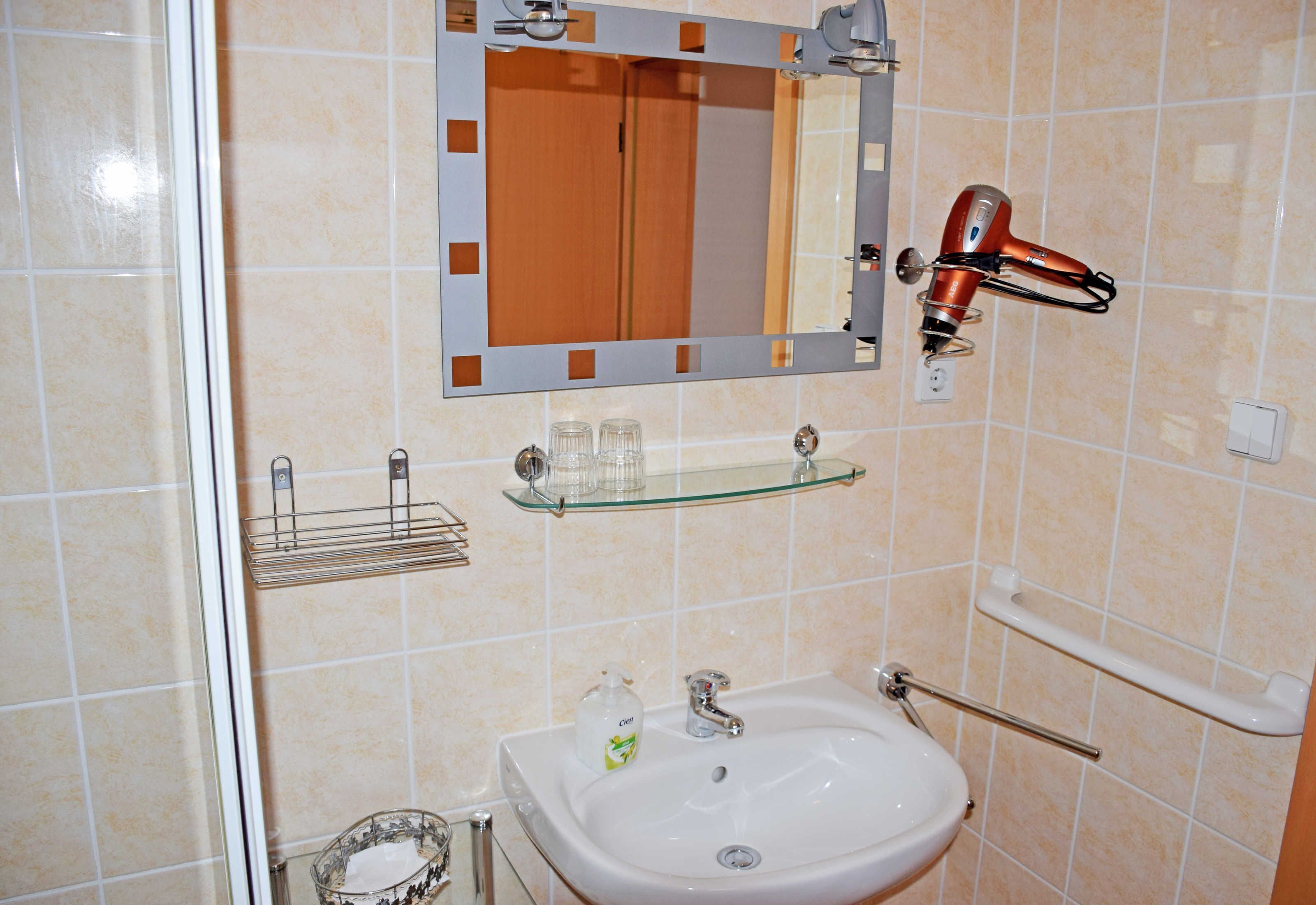 A bathroom with a white sink, a mirror, a hairdryer, and a glass shelf.