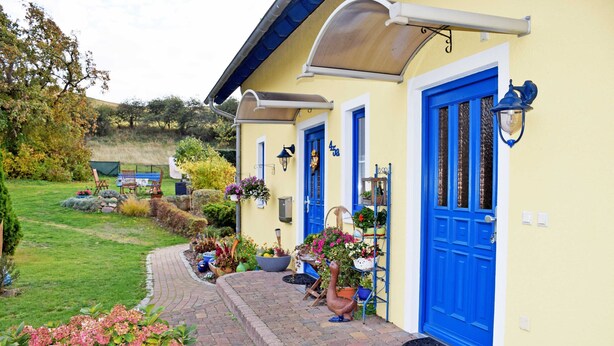 A yellow building with blue doors and windows, a paved pathway, and various potted plants. - Vacation apartment Mönchgut - Holiday apartments in Gager on Rügen (Gager)
