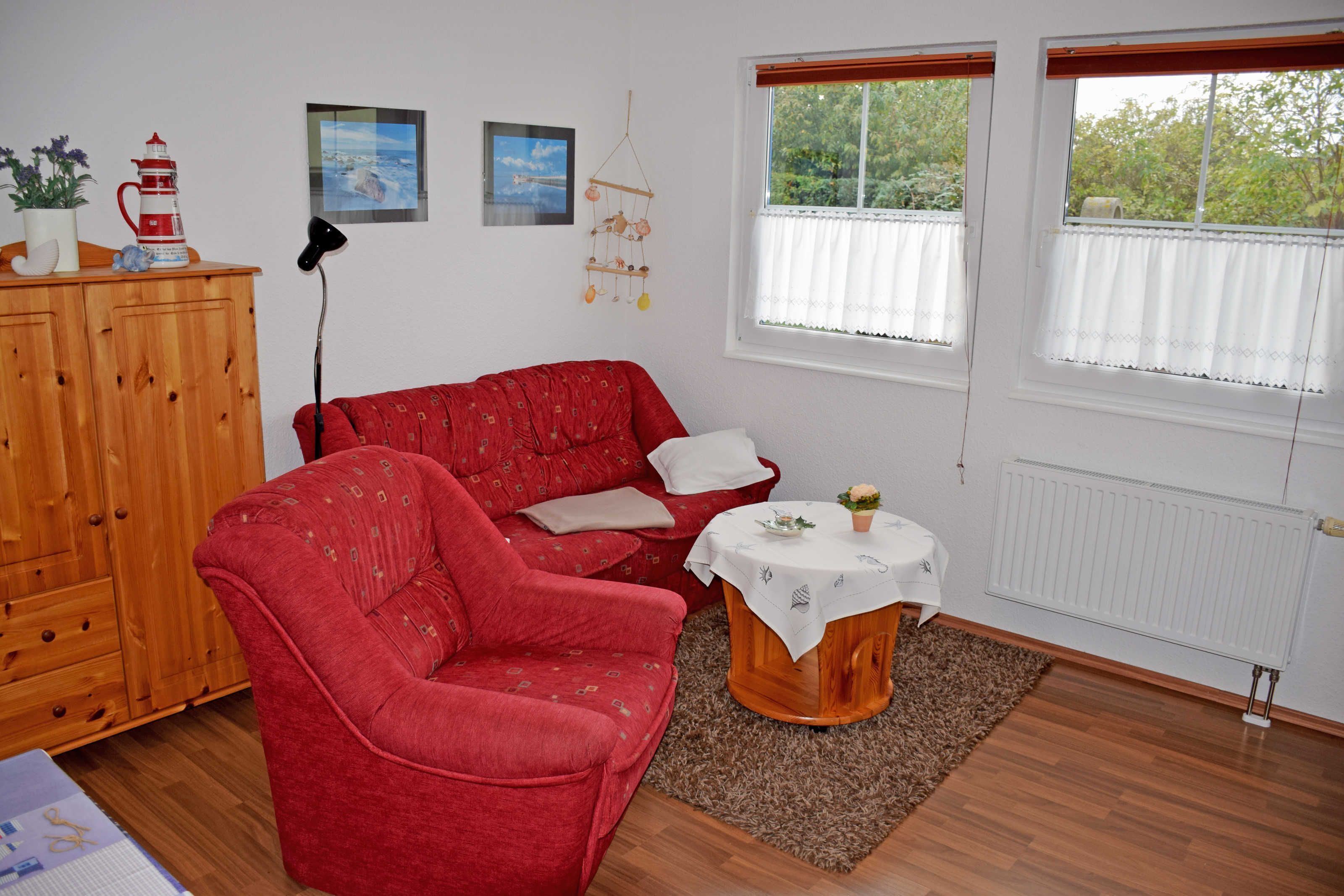 Un canapé rouge, une petite table ronde, un meuble en bois et une fenêtre avec des rideaux.