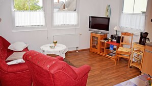 A living room with a red sofa, a television, a small table with a vase, and a cabinet with books and a coffee maker. - Vacation apartment Mönchgut - Holiday apartments in Gager on Rügen (Gager)