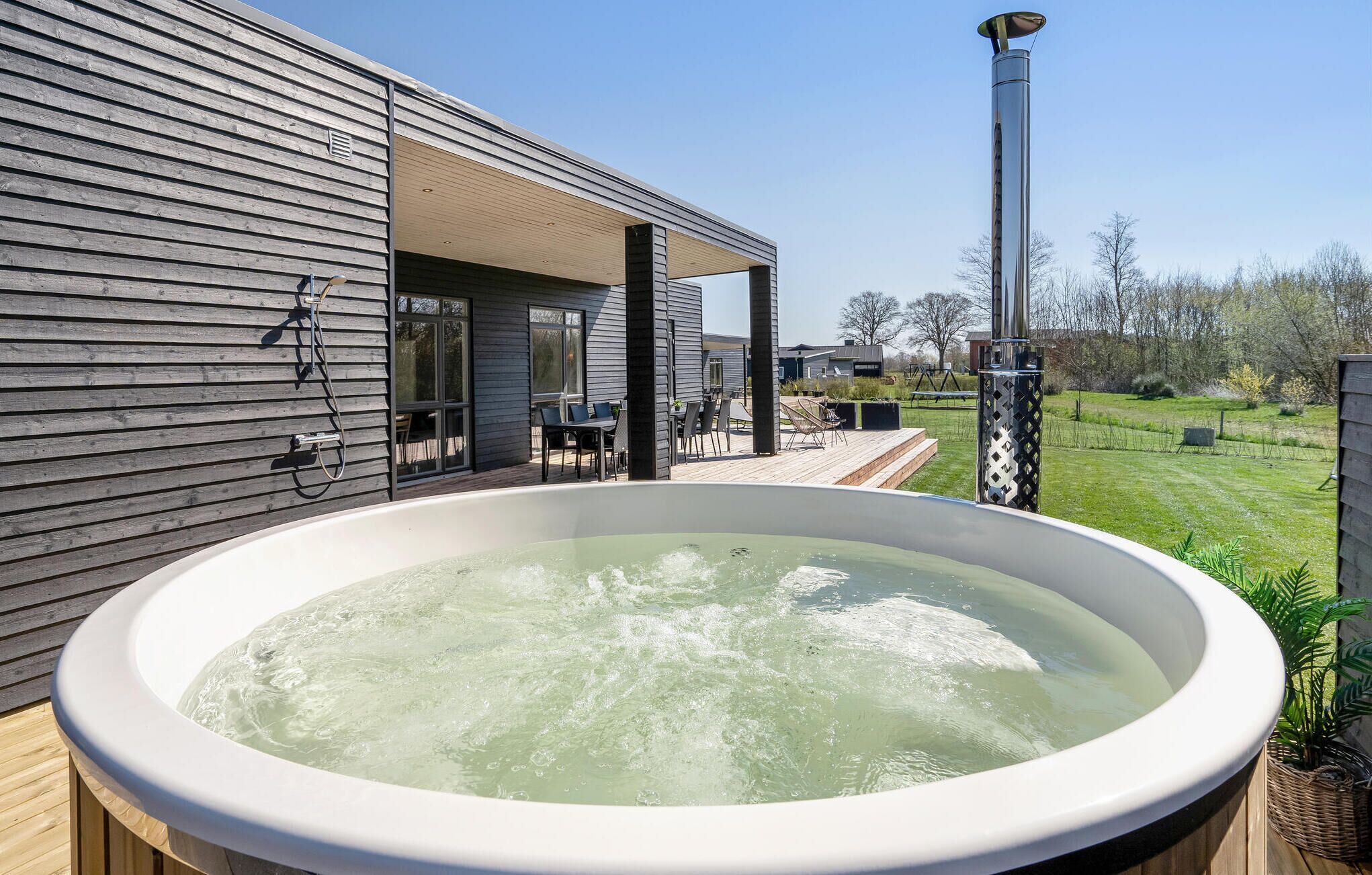 A hot tub outside a modern house with a wooden deck and a clear sky.