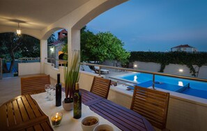 Un espace extérieur aménagé pour les repas, avec une piscine, des meubles en bois et une vue sur un bâtiment en arrière-plan.