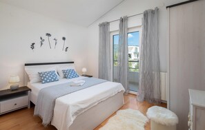 Une chambre à coucher avec un lit, des tables de chevet, une lampe, un tapis moelleux et une vue sur l’extérieur.