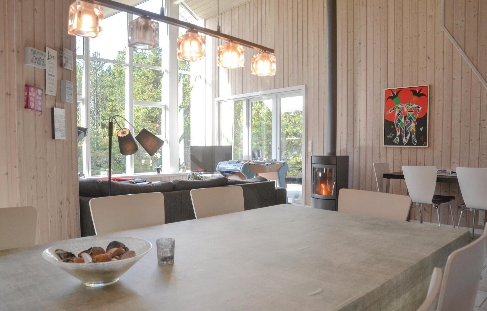 A cozy room with a wooden interior, a foosball table, a fireplace, and a large window offering a view of trees.