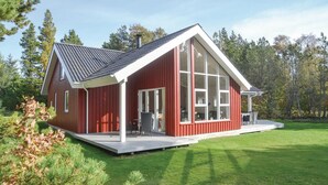 A red cabin with a large glass window, a deck, and a sloped roof. - Cozy home in Oksbøl with sauna (Oksbøl)