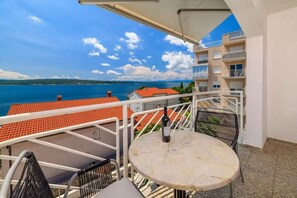 A balcony with a table and chairs, overlooking a body of water and buildings. - Holiday apartment with communal pool and balcony (Crikvenica)