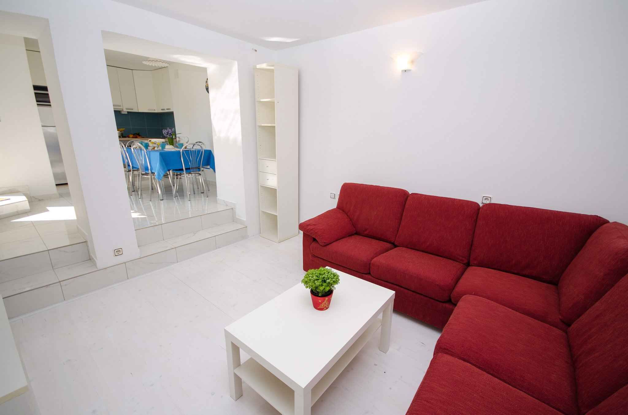 A modern living room with a red sofa, a white coffee table, and a dining area in the background.