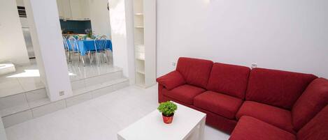 A modern living room with a red sofa, a white coffee table, and a dining area in the background.