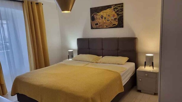 A bedroom with a bed, nightstands, a lamp, and a painting on the wall. - Holiday apartment with terrace (Crikvenica)