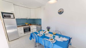 A compact kitchen with white cabinets, a microwave, and a dishwasher. A blue table is set with plates, cups, and a vase of flowers. - Holiday apartment with terrace (Crikvenica)