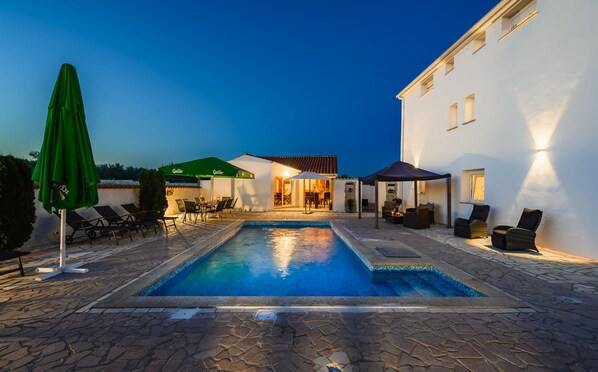 Una piscina con lettini e ombrelloni, una veranda coperta e un edificio con tetto in tegole.
