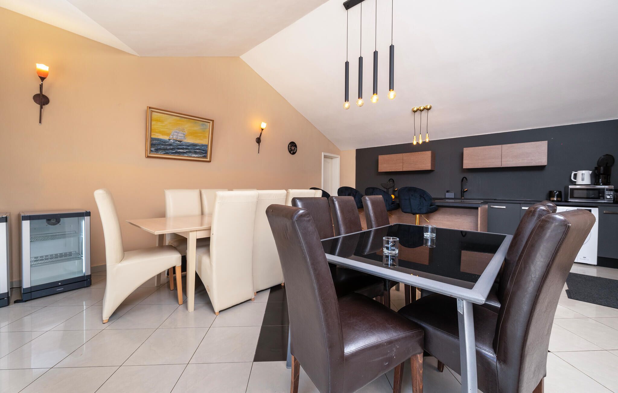 A modern dining area with a glass-top table, leather chairs, and pendant lighting.