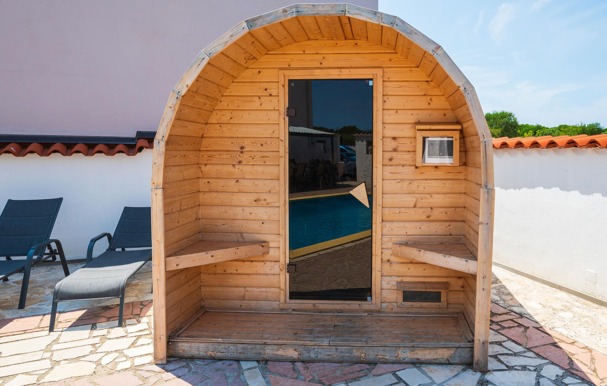 Un sauna en bois avec une porte, une petite fenêtre et une piscine visible à travers la porte.