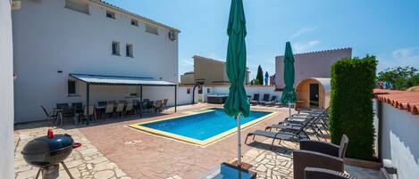 A pool area with lounge chairs, a barbecue grill, and a covered seating area.