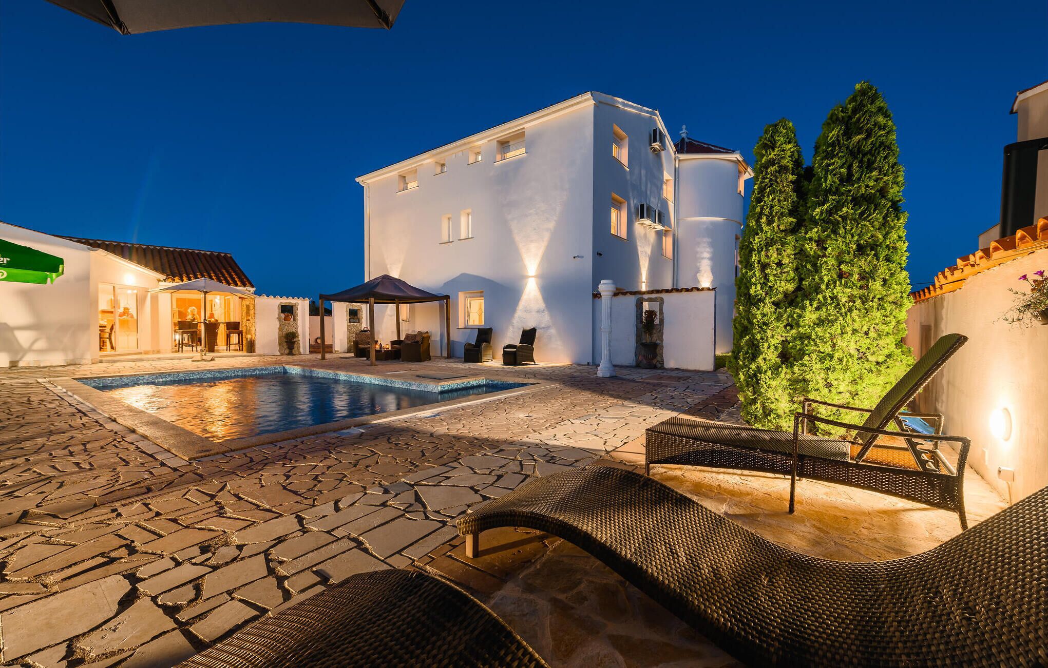 Ein Poolbereich mit Liegestühlen, ein Gebäude mit vielen Fenstern und ein gepflegter Garten.
