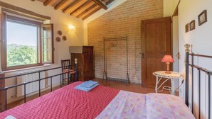 A bedroom with a large bed, a window, a wooden wardrobe, a metal chair, a small table with a lamp, and a brick wall. - Pet friendly apartment (S.Vito In Monte TR)