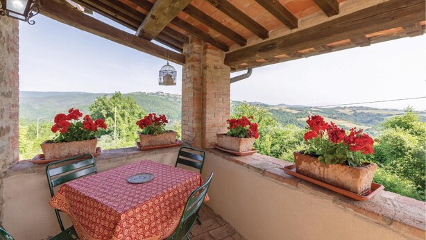 A covered outdoor seating area with a table and chairs, surrounded by potted red flowers, overlooking a scenic landscape. - Pet friendly apartment (S.Vito In Monte TR)