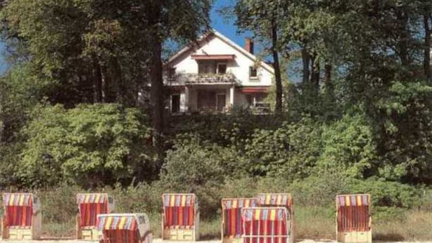 A house with a balcony, surrounded by dense trees. - 3-room apartment, 80 m², balcony, sea view - Haus am Hang Pension garni (Scharbeutz)