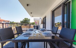 Ein Balkon mit einem Glastisch, gedecktem Esstisch, Korbstühlen und Blick auf die Umgebung.