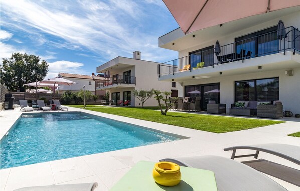 Ein modernes, zweistöckiges Haus mit Swimmingpool, Außenbereich zum Sitzen und einem gepflegten Rasen.