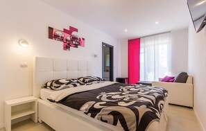 Ein modernes Schlafzimmer mit Bett, Nachttischen, einer Couch und einem Fenster mit Vorhängen.