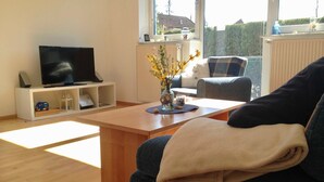 A modern living room with a flat-screen TV, a coffee table, a sofa, and a view of the outdoors. - Baltic Sea residence, App. 2 - Biting Resence 2-Zi.-Fewo., EC (Neustadt in Holstein)
