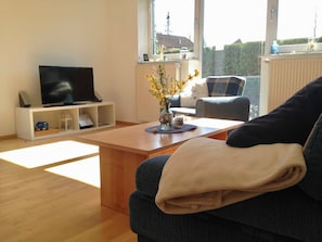 A modern living room with a flat-screen TV, a coffee table, a sofa, and a view of the outdoors. - Baltic Sea residence, App. 2 - Biting Resence 2-Zi.-Fewo., EC (Neustadt in Holstein)