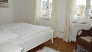 Un dormitorio con cama, una silla, un ventanal y un radiador.