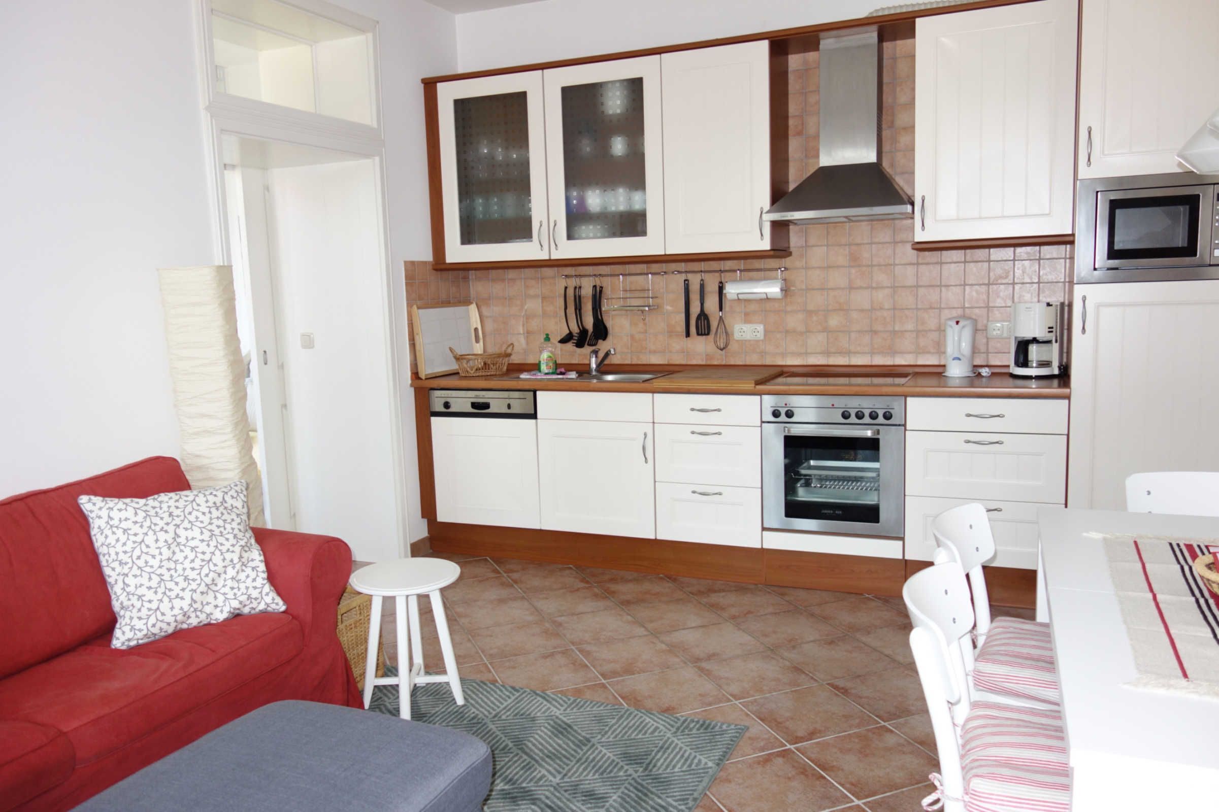 A compact kitchen with white cabinets, a microwave, and a stove. There is a red sofa and a small white table with a striped tablecloth.