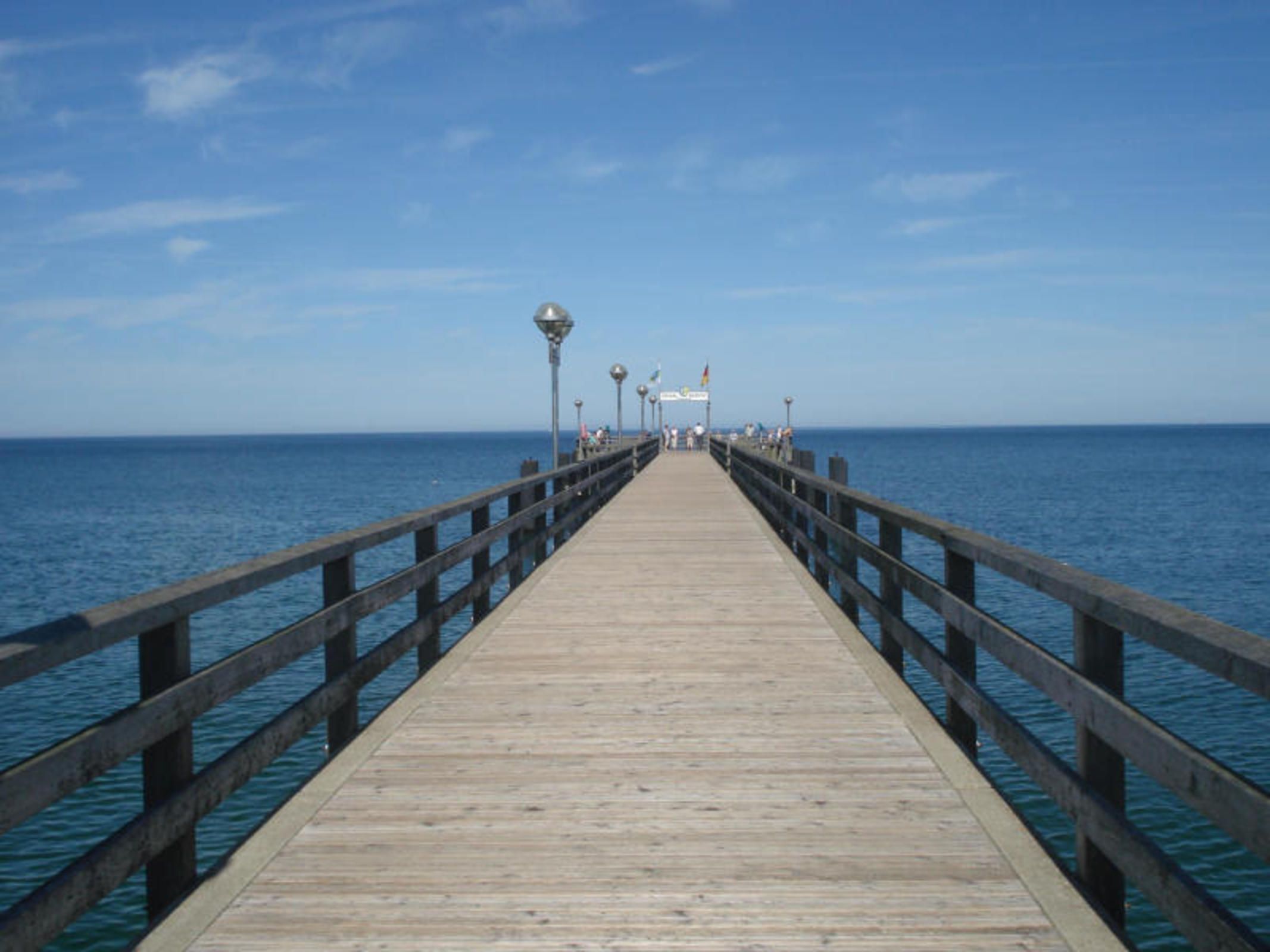 A wooden pier extending into the sea with railings on both sides.