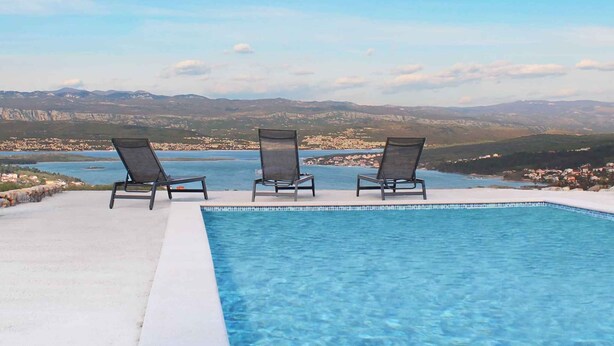 A swimming pool with three lounge chairs facing a scenic view of a coastal town and mountains. - Holiday apartment with pool and sea view (Čižići)
