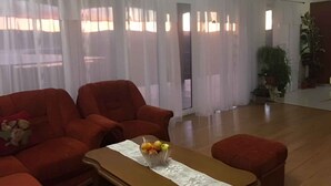 A living room with a sofa set, a coffee table with fruit, and a view through sheer curtains. - Holiday apartment with pool and sea view (Čižići)