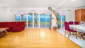 A spacious room with a red sofa, a dining table with chairs, and large windows offering a view of the countryside. - Holiday apartment with pool and sea view (Čižići)