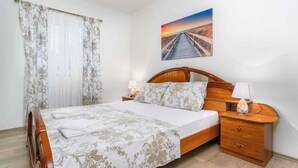 A neatly made bed with a floral bedspread, a wooden headboard, and two bedside lamps. - Holiday apartment with pool and sea view (Čižići)
