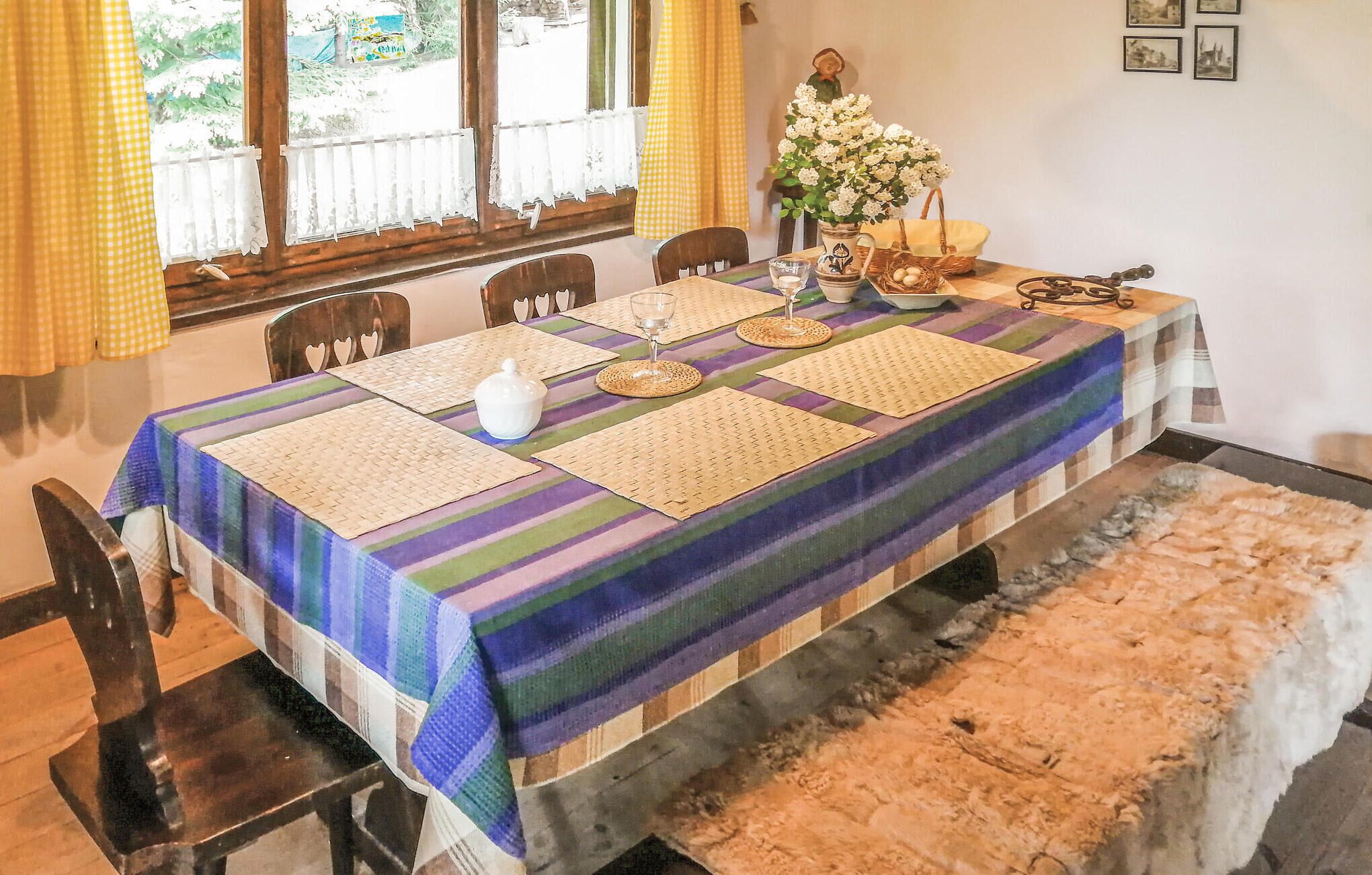 A dining table set with placemats, a vase of flowers, and a basket with eggs.