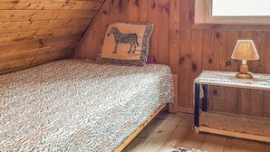 A cozy room with a bed, a zebra-patterned pillow, a small table with a lamp, and wooden walls.