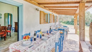 A covered dining area with a long table set for a meal, wooden beams on the ceiling, and a view of the outdoors. - 6 bedroom beautiful home in Orosei NU (Orosei NU)