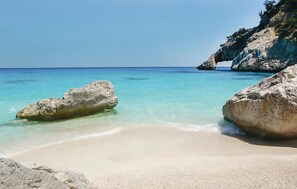 Una spiaggia con acque cristalline color turchese, grandi rocce e una battigia sabbiosa.