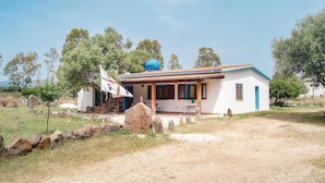 A single-story house with a tiled roof, a porch, and a flagpole with a flag. - 6 bedroom beautiful home in Orosei NU (Orosei NU)