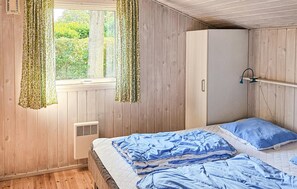 A bedroom with wooden walls, a bed with blue bedding, a wardrobe, and a window with curtains. - Pet friendly home in Glesborg with sauna (Glesborg)
