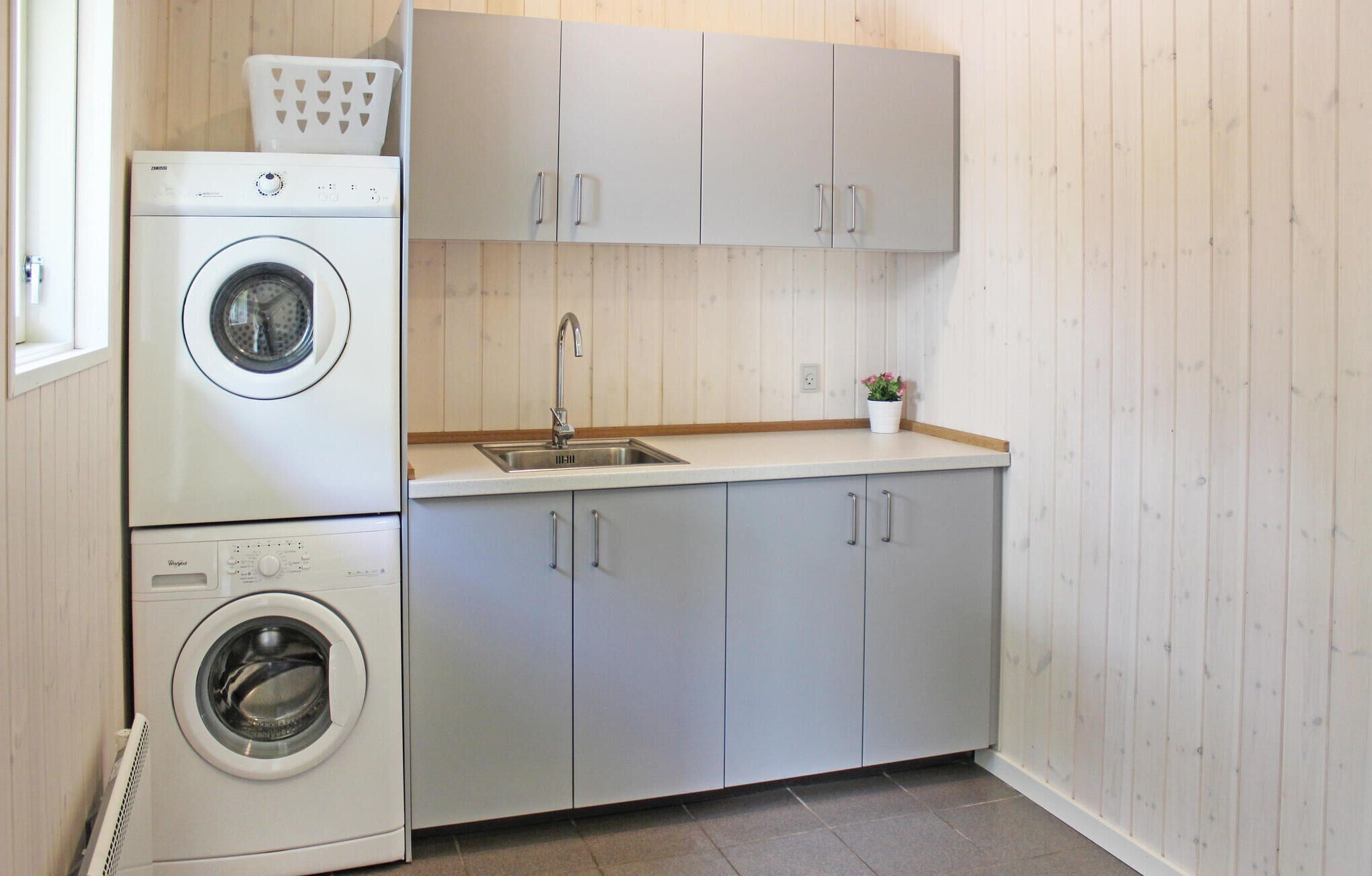 A compact laundry room with two washing machines, a sink, and light wooden cabinets.
