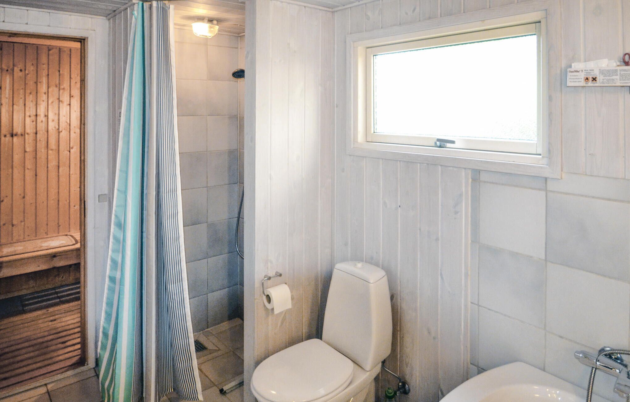 Une salle de bain avec une porte en bois, une douche avec un rideau, des toilettes et une fenêtre.