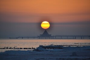 A sunset over a body of water with a pier and a building in the background. - Category I, EC, 2 P. - Apartments Villa "On the sunny beach" (Heringsdorf)