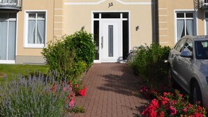 A building with a beige facade, a white door, and the number 13. There are plants and a car in front. - Category I, EC, 2 P. - Apartments Villa "On the sunny beach" (Heringsdorf)