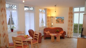 A furnished living room with a dining table, chairs, a sofa, and a small table with a vase. - Category I, EC, 2 P. - Apartments Villa "On the sunny beach" (Heringsdorf)
