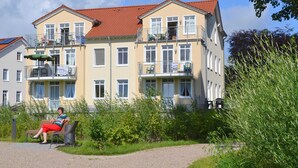 A multi-story building with balconies, a person sitting on a bench, and greenery around. - Category I, EC, 2 P. - Apartments Villa "On the sunny beach" (Heringsdorf)