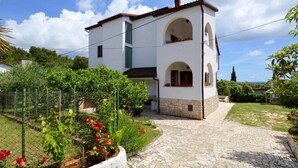 A two-story house with a stone pathway leading to the entrance, surrounded by a garden with various plants and flowers. - Holiday apartment with air conditioning and balcony (Premantura)